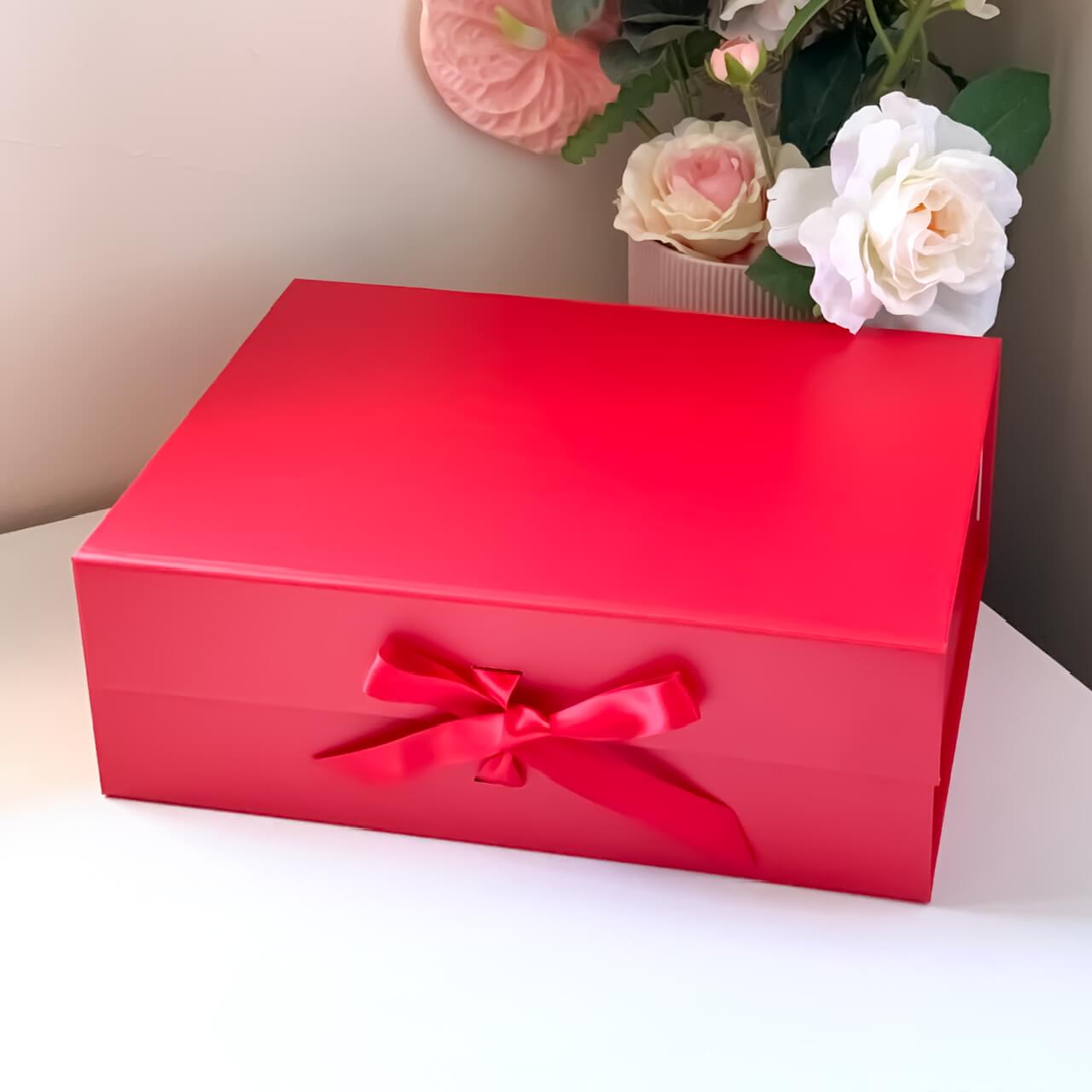 Red gift box with a bow on a white surface with flowers in the background